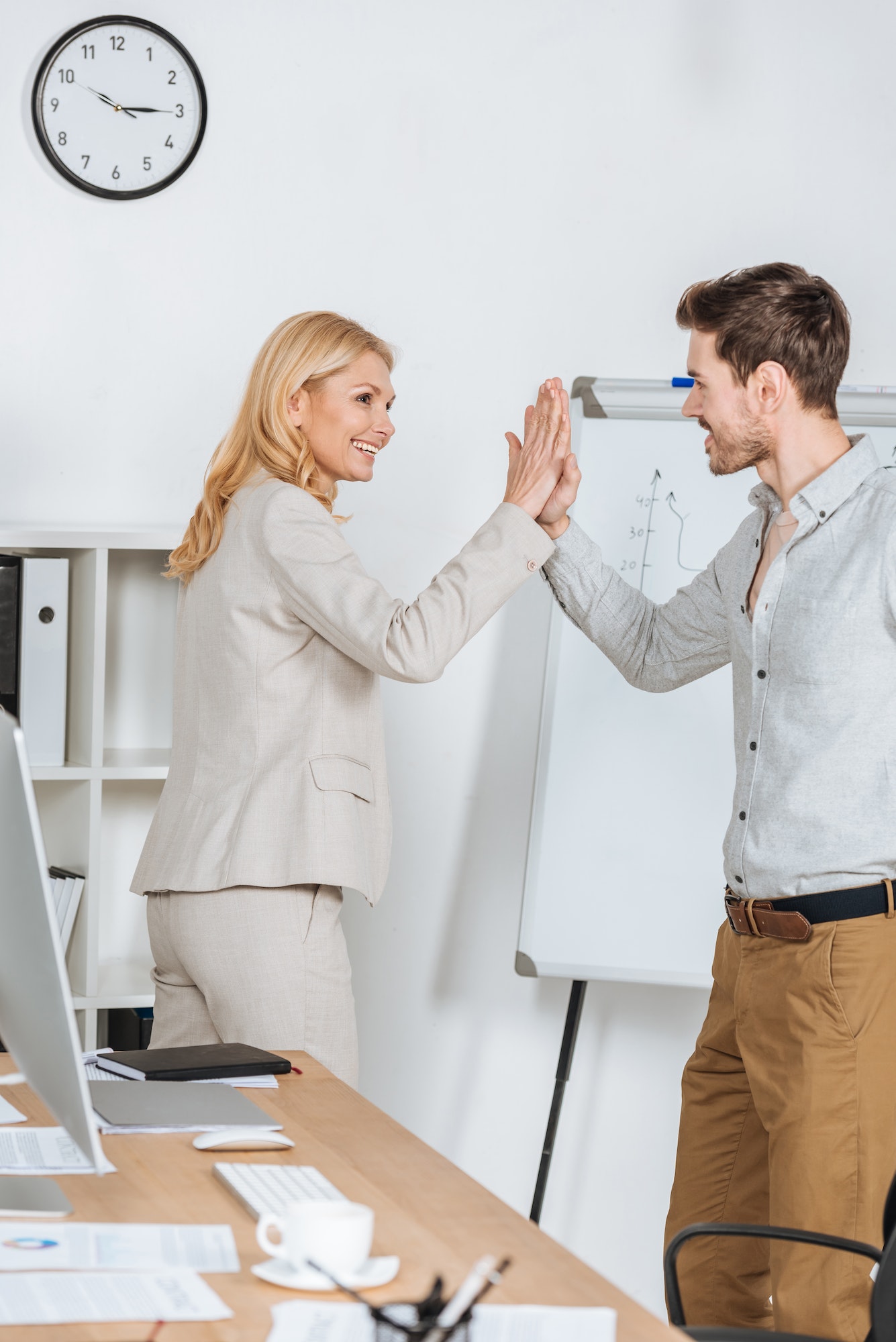 happy businessman and businesswoman smiling and giving high five in office