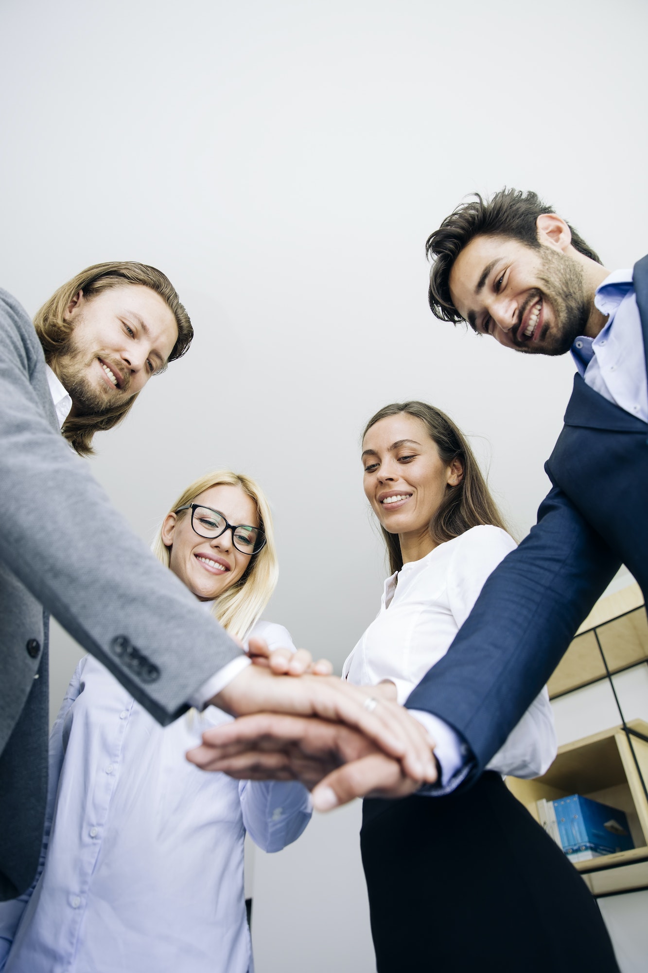 Young coworkers putting hands together as symbol of unity in the office